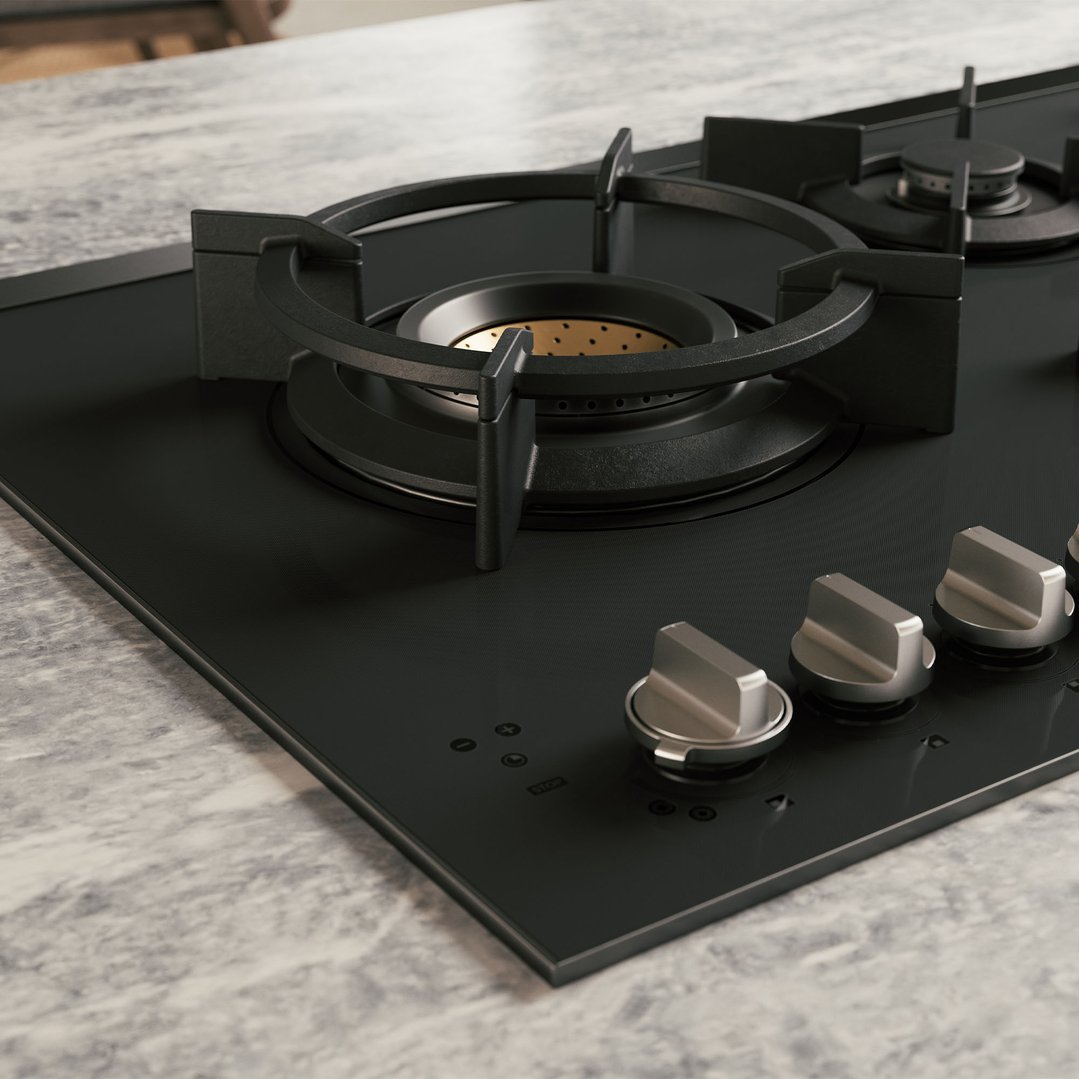 Close up of a black gas cooktop with five burners on a marble countertop