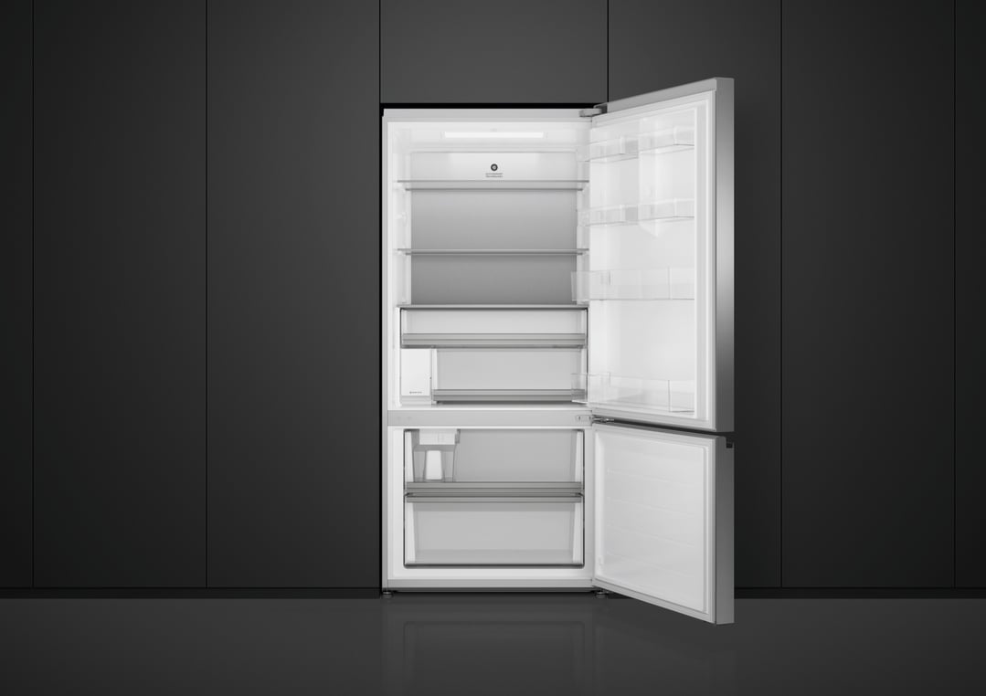 Open refrigerator freezer with interior lights on in a dark kitchen