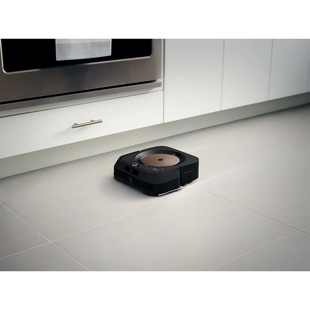 Black robot mop cleaning a tiled kitchen floor under white cabinets