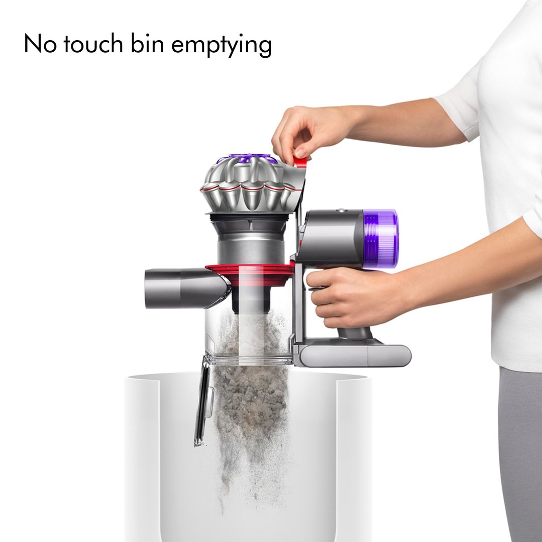 Hand emptying a Dyson handstick vacuum cleaner into a bin, showing dust falling