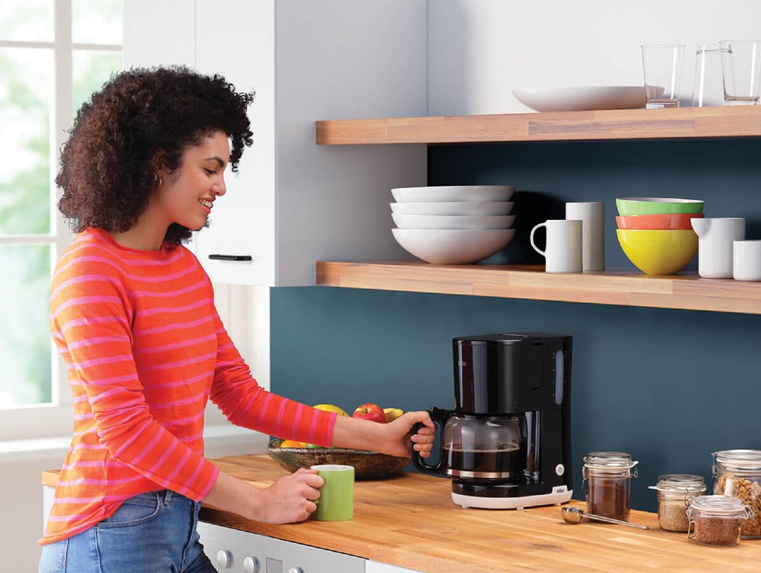 Woman holding a green mug and coffee pot in a modern kitchen