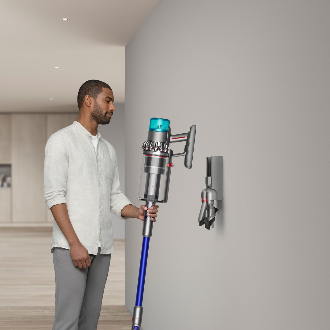 Man holding a Dyson handstick vacuum in a modern home setting