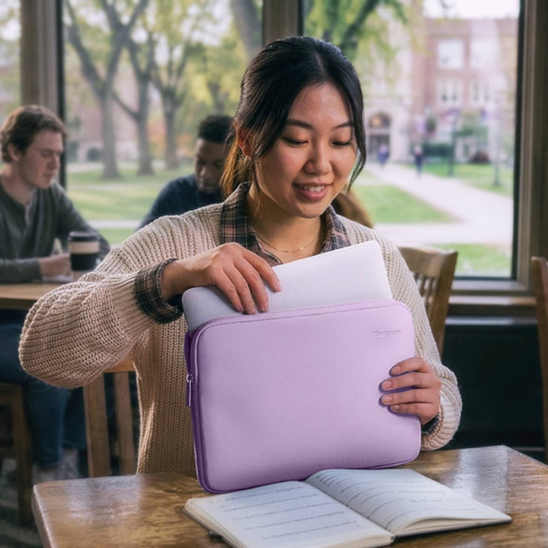 Woman putting a white laptop into a purple laptop sleeve at a wooden table
