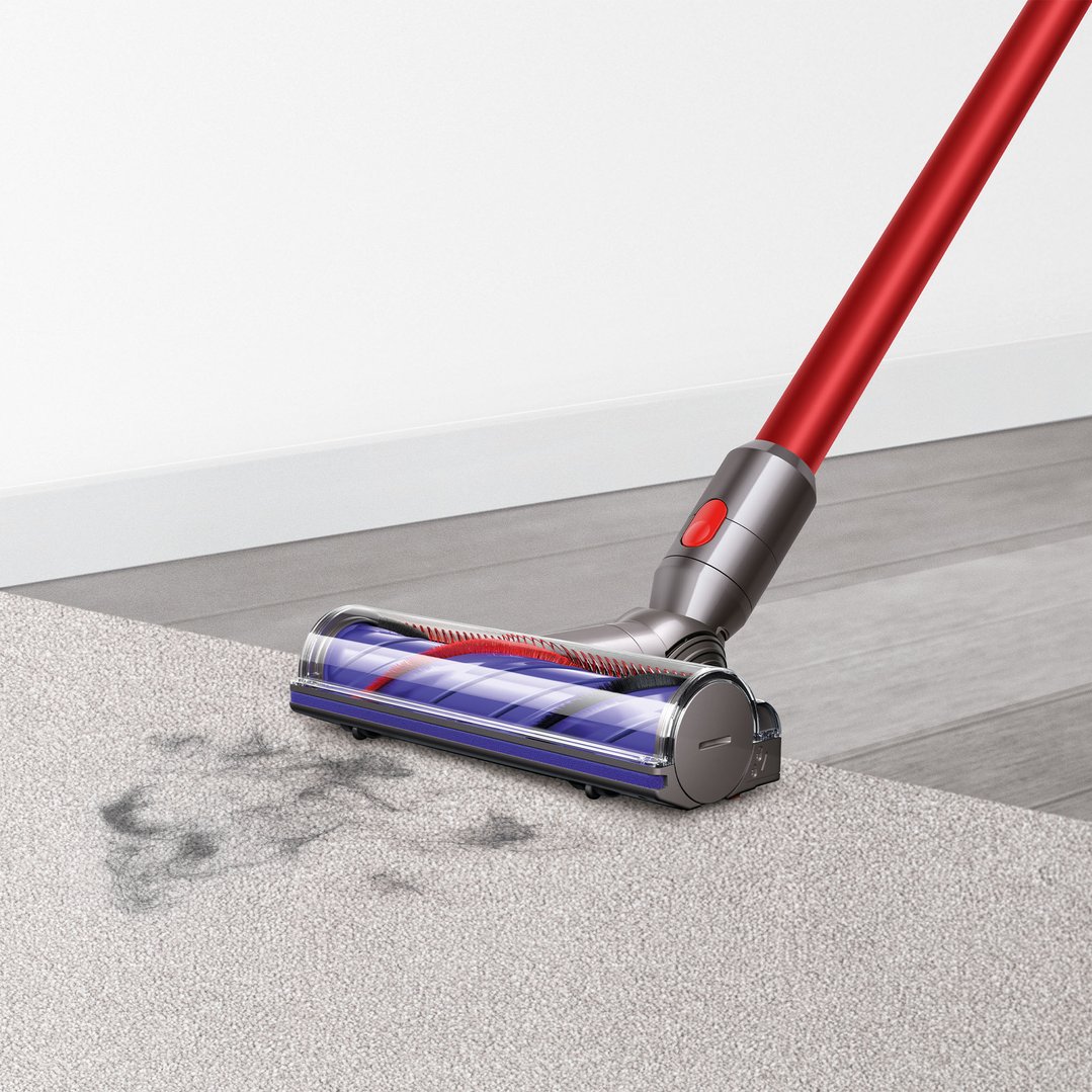Dyson handstick vacuum cleaning dirt from a light grey carpet