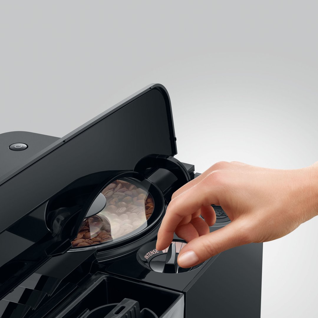 Hand adjusting the intensity dial on a JURA coffee machine with coffee beans visible