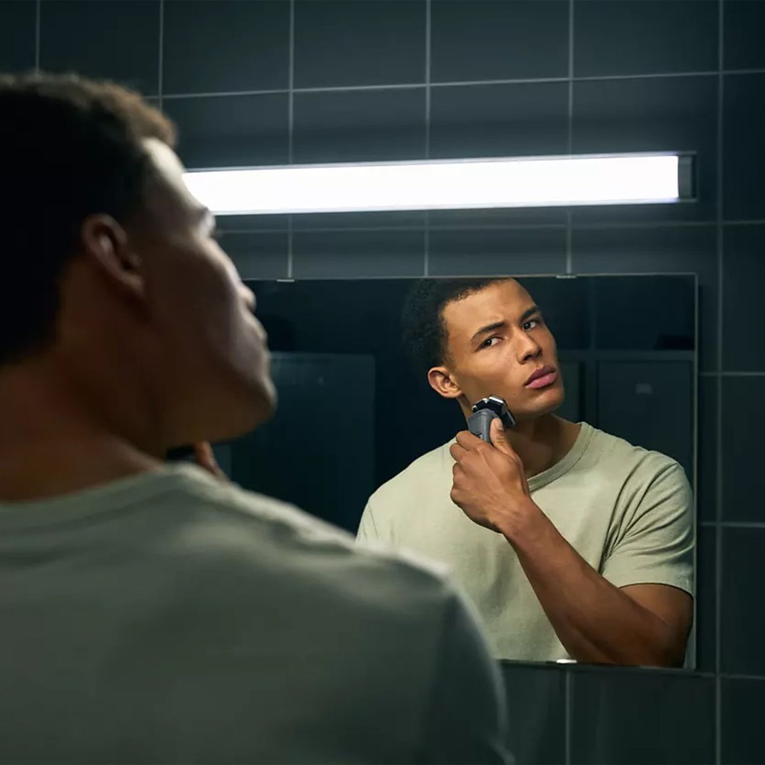 Man shaving with a shaver in front of a mirror in a bathroom
