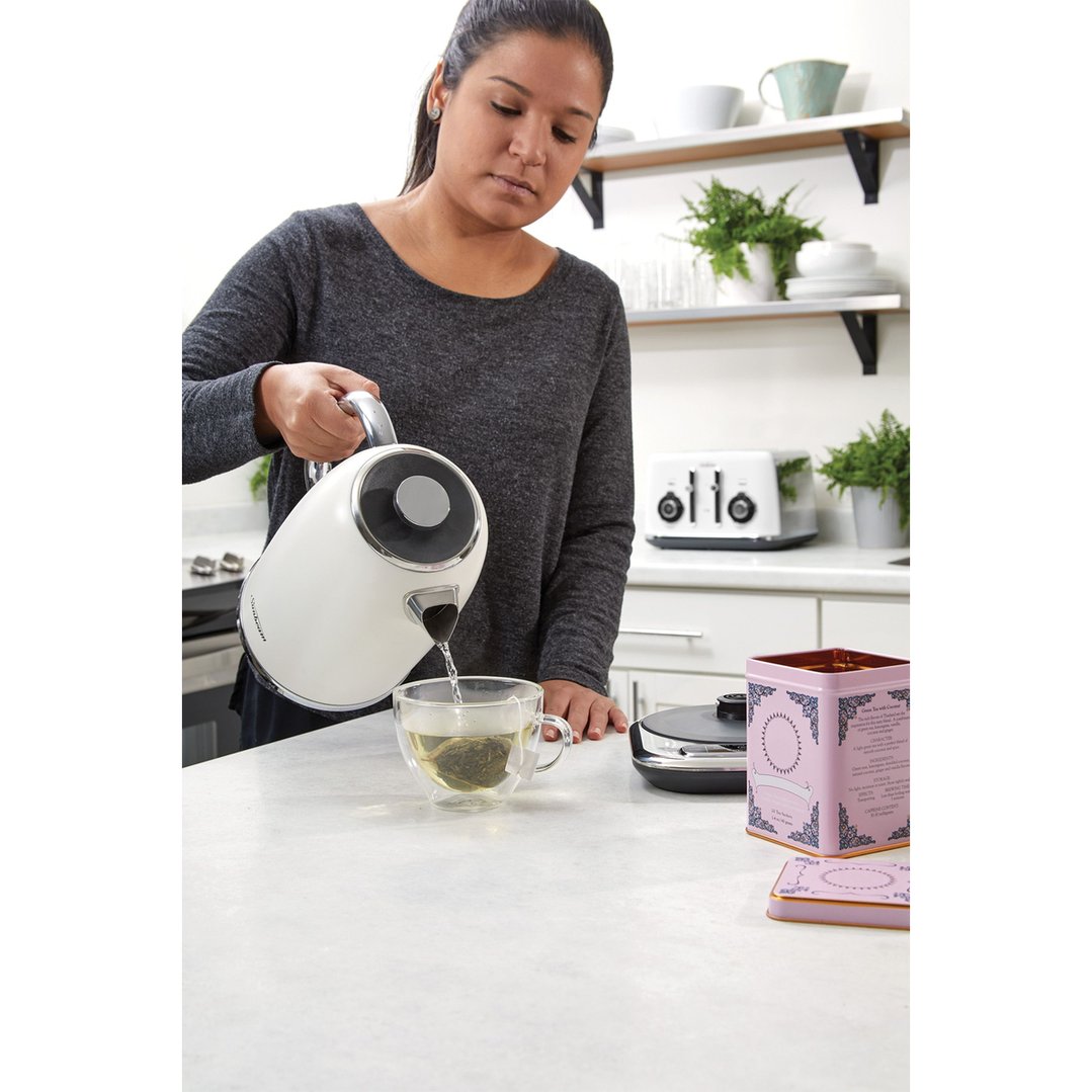 Woman pouring hot water from a white kettle into a glass cup of tea