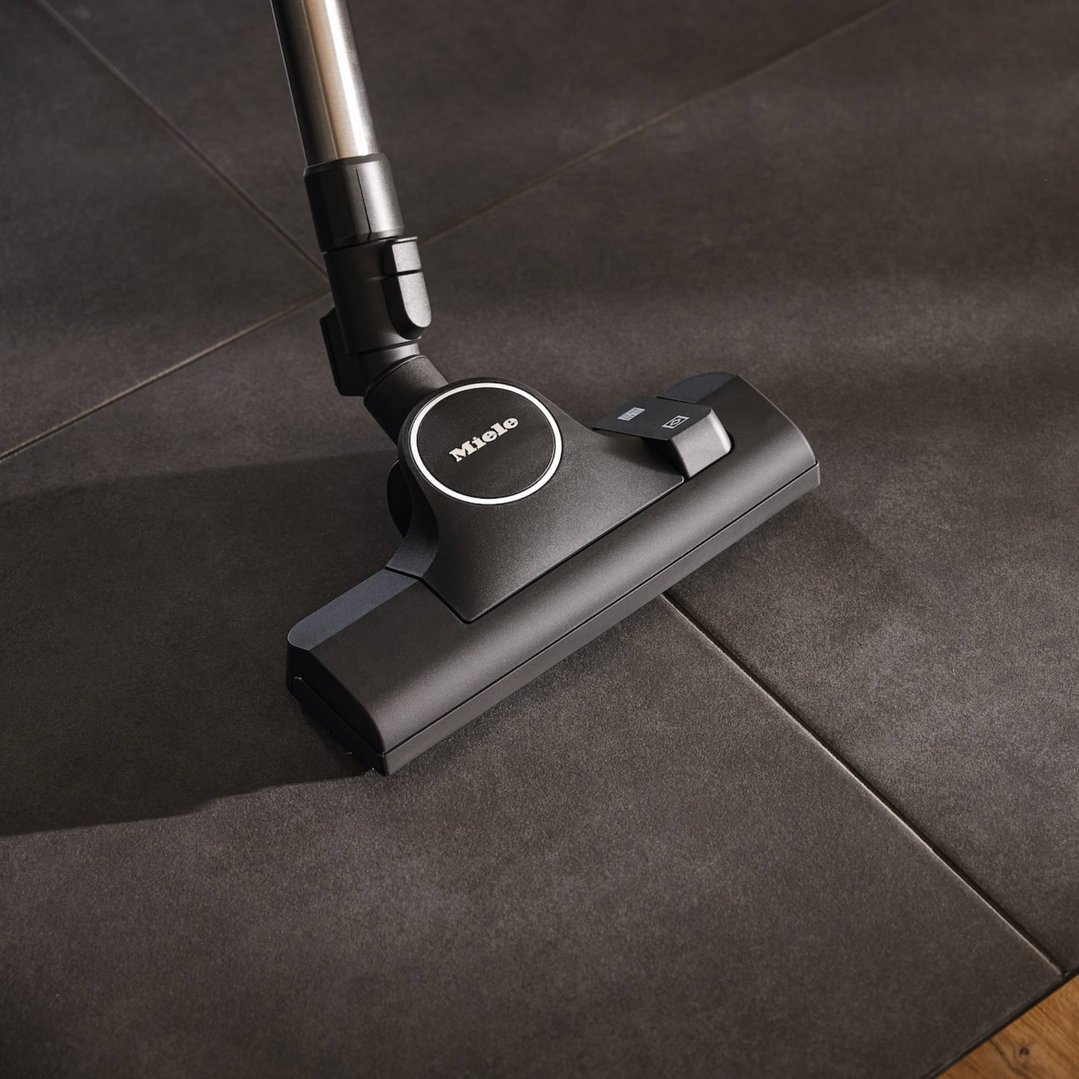 Vacuum cleaner floorhead on a dark tiled floor, angled view