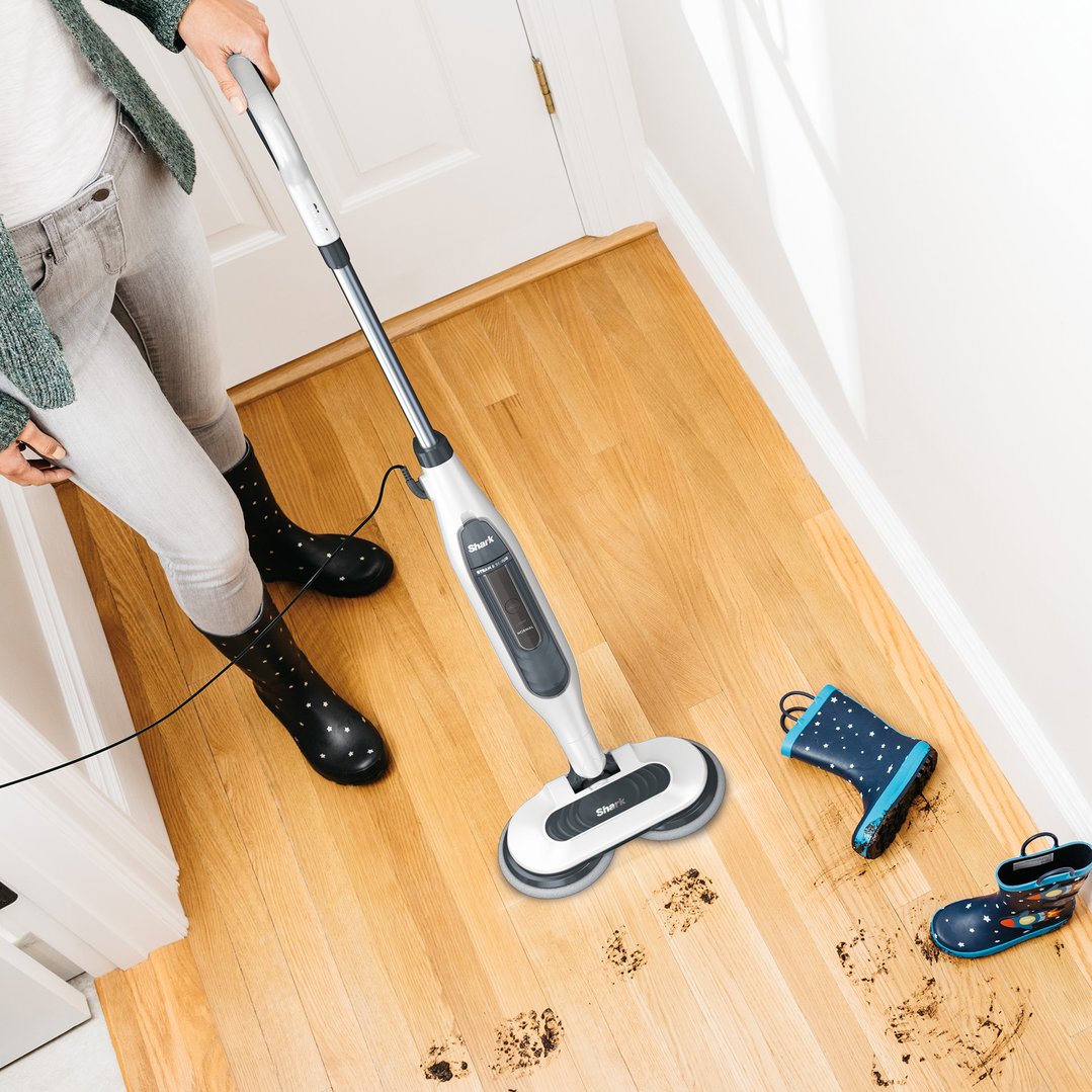 Person in rain boots cleaning muddy footprints on a wooden floor with a steam mop