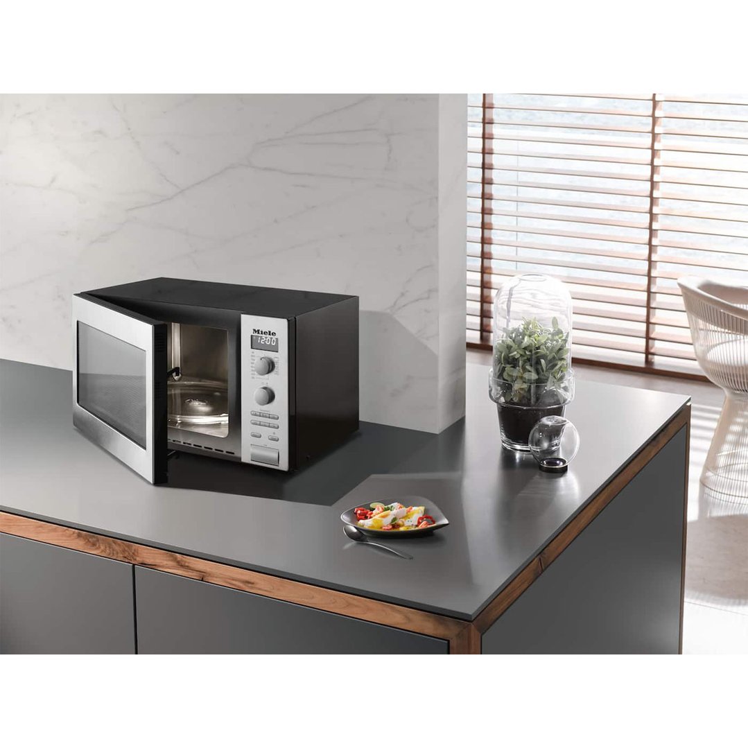 Benchtop microwave oven with door open on a kitchen counter with decor and food