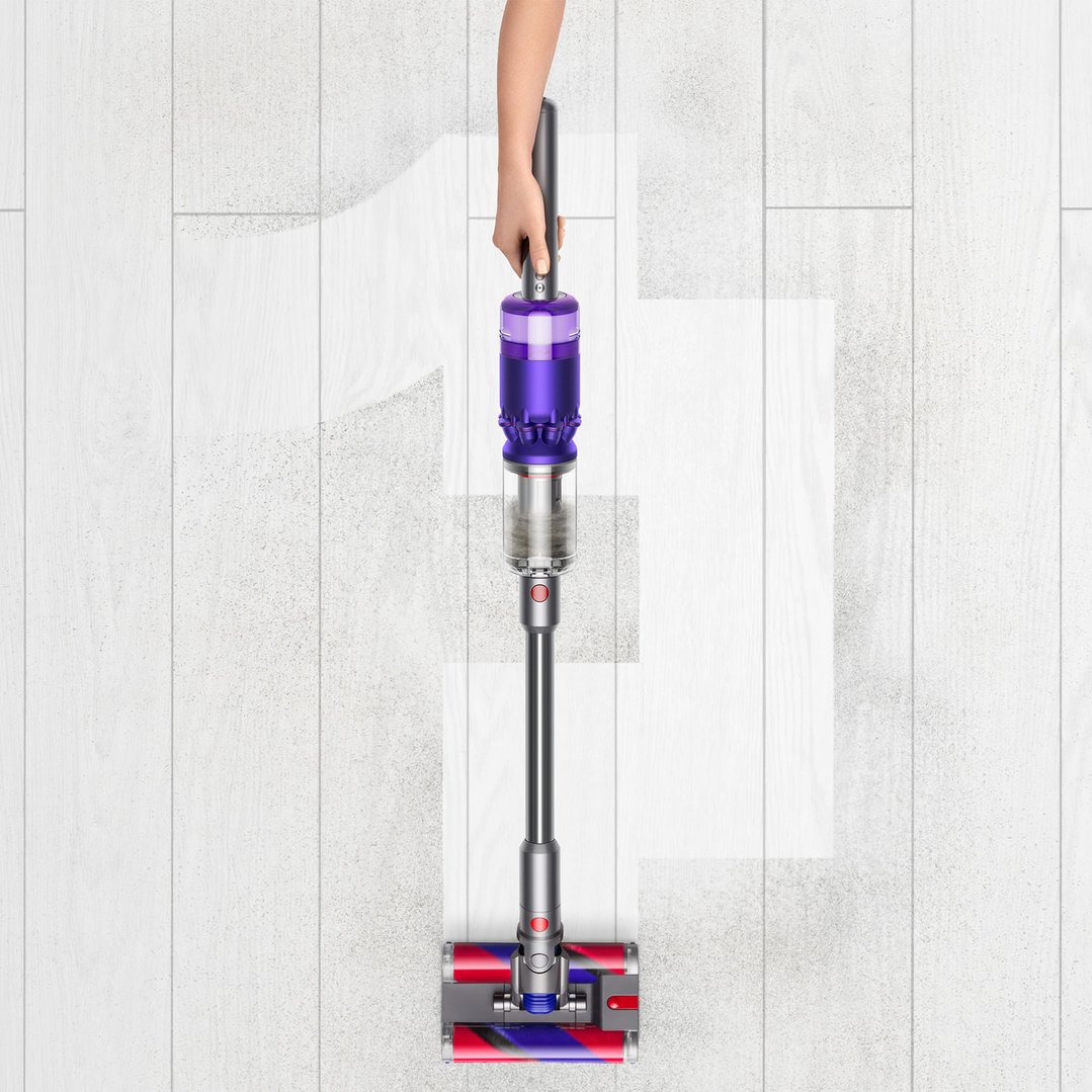 Hand holding Dyson Omni-glide Stick Vacuum cleaning a dirty white wooden floor