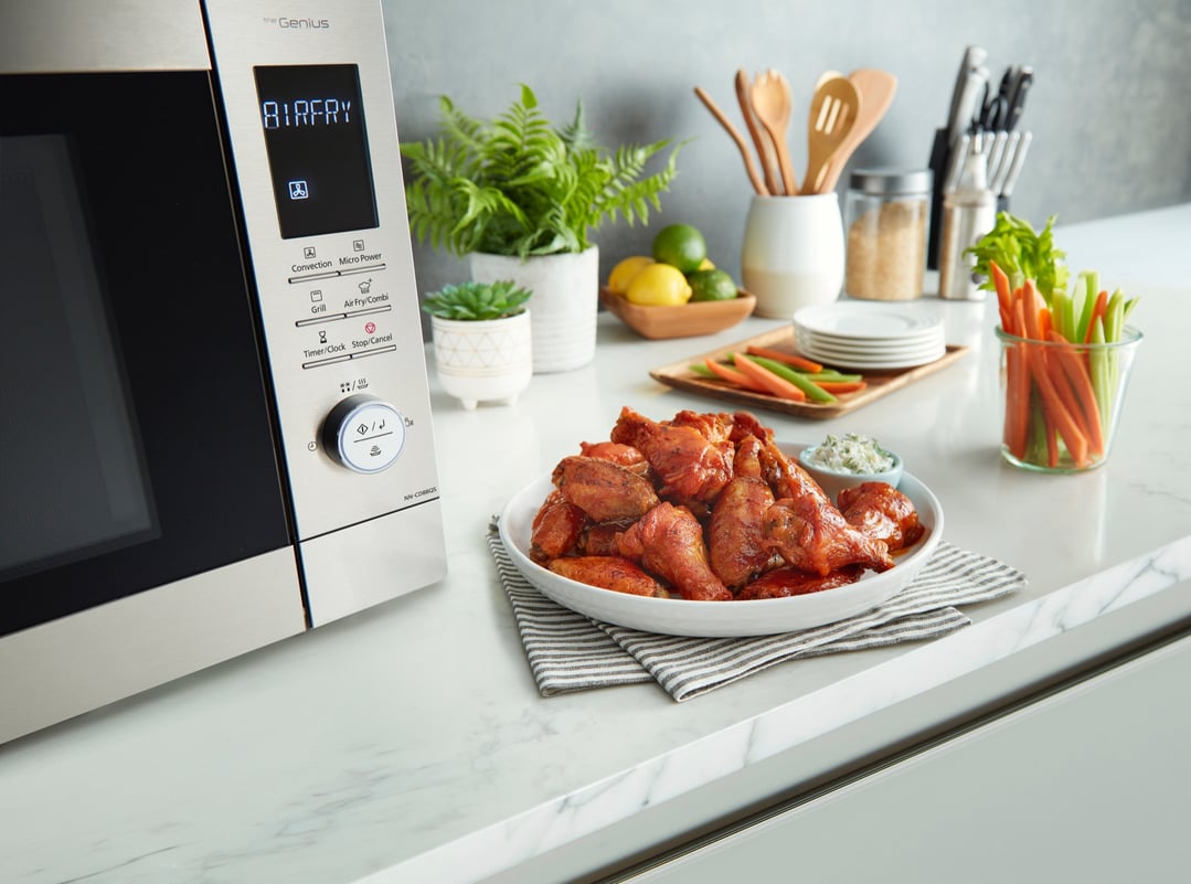A Panasonic microwave oven on a kitchen counter with chicken wings and vegetables