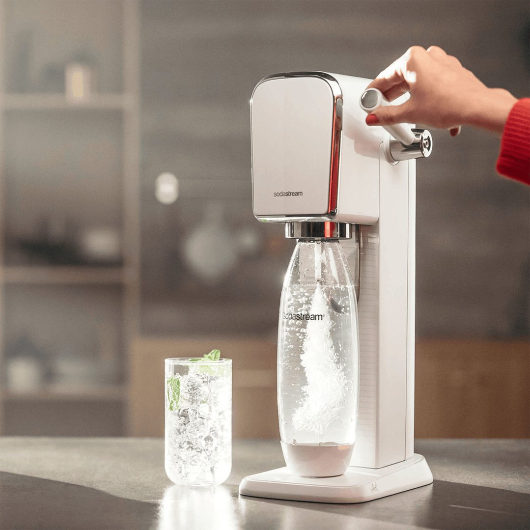 Hand operating a white SodaStream Art Sparkling Water Maker, with a glass of water