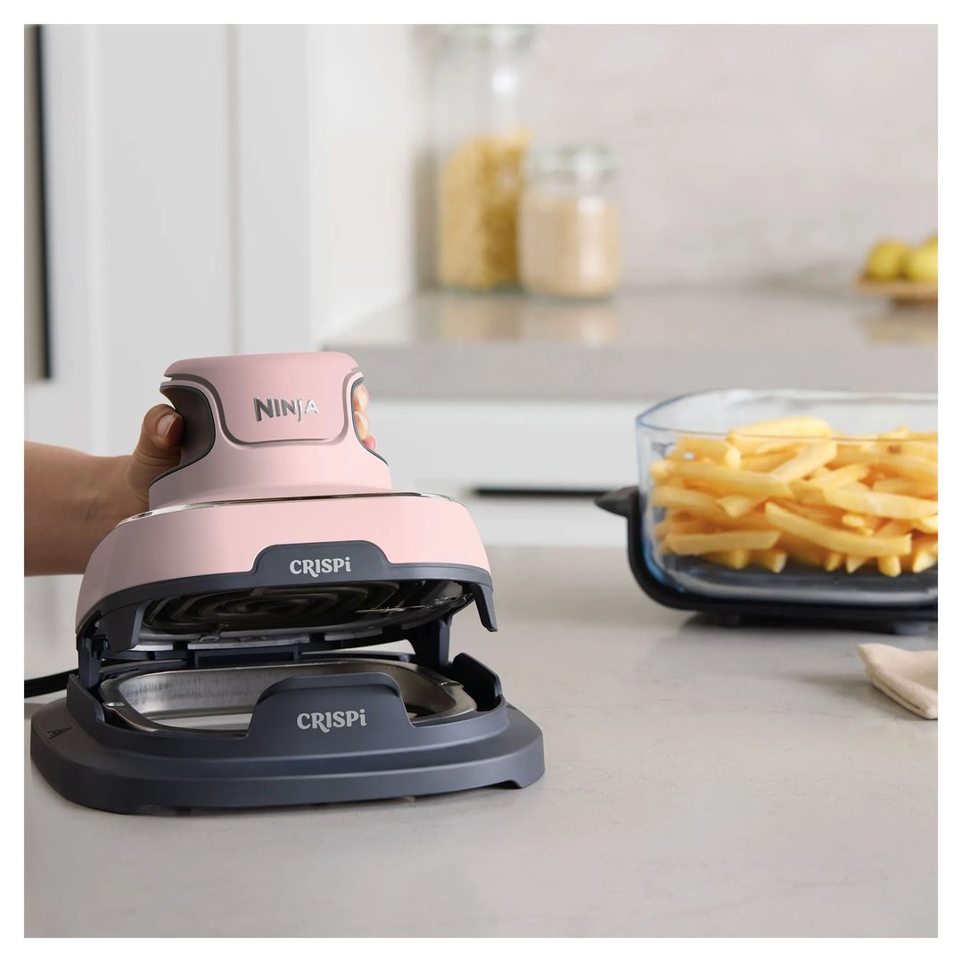 Hand opening a pink Ninja Crispi air fryer on a kitchen counter with fries