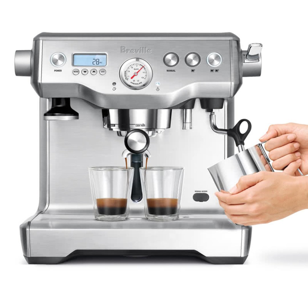 Hands steaming milk while coffee brews into two glasses on a Breville coffee machine