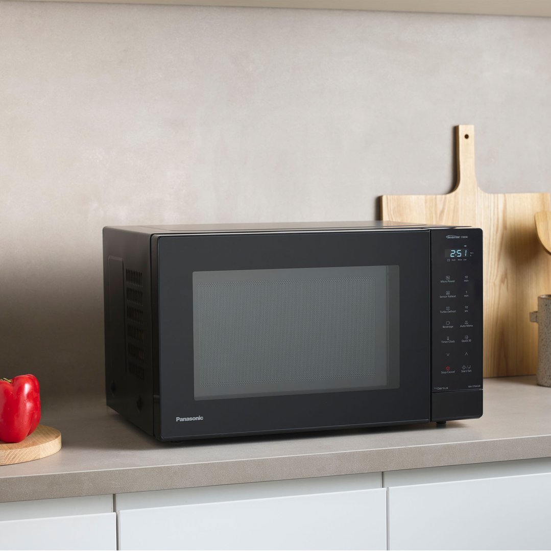 Black Panasonic microwave on a kitchen counter with cutting boards and a pepper