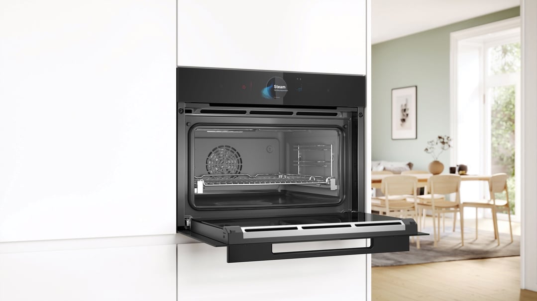Built-in compact oven with steam function with its door open in a kitchen setting