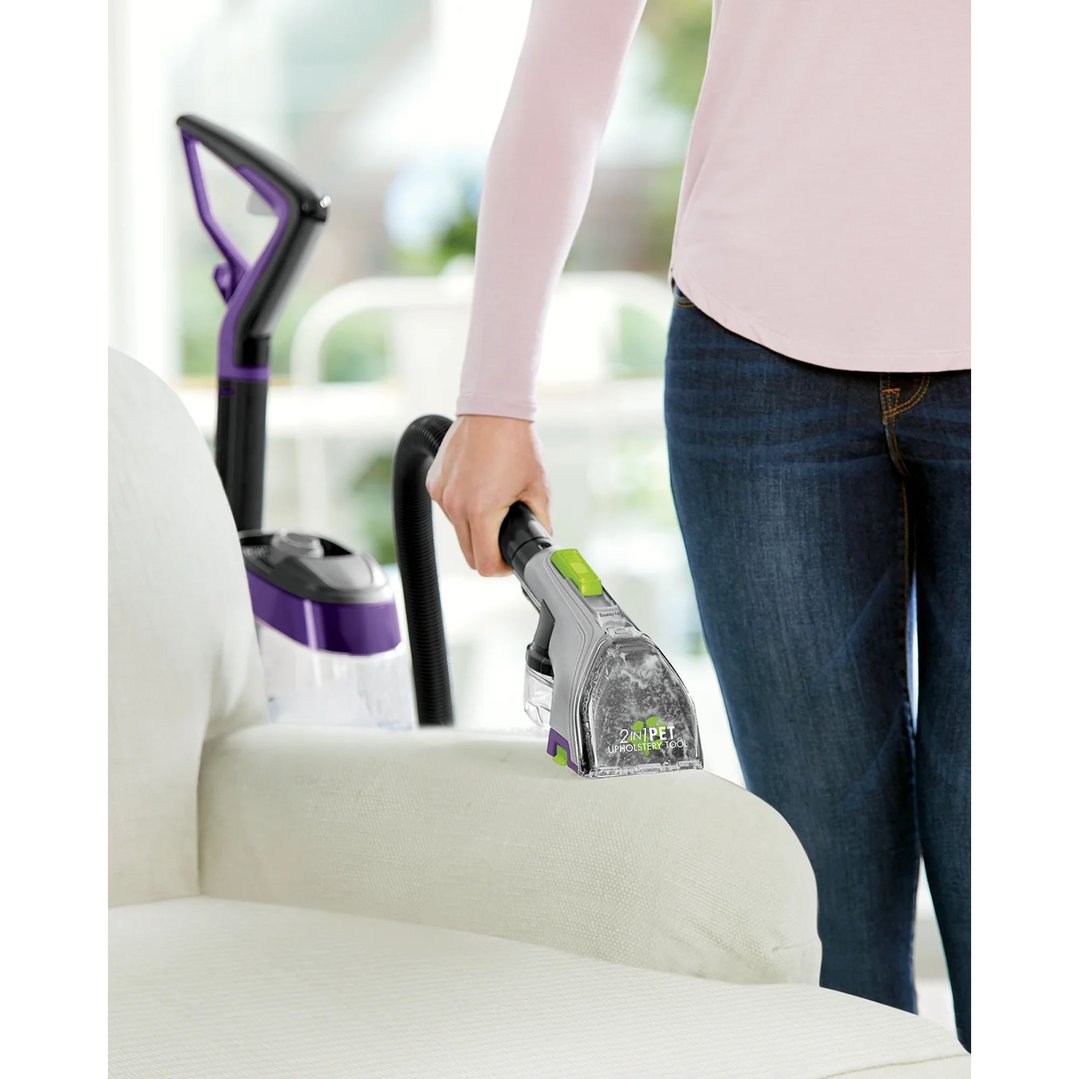 Woman using a BISSELL carpet washer attachment to clean a white sofa