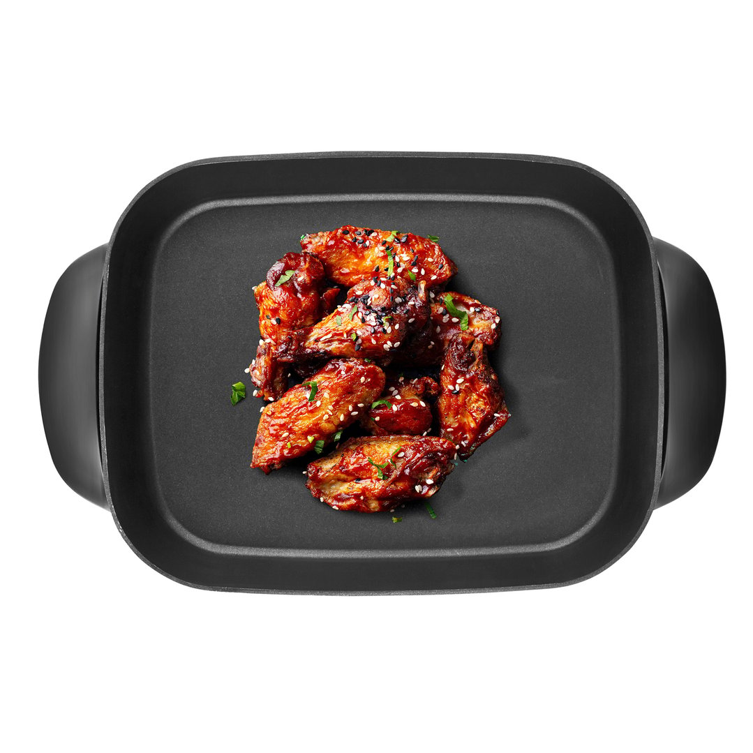 Top-down view of chicken wings in an electric frypan on a white background