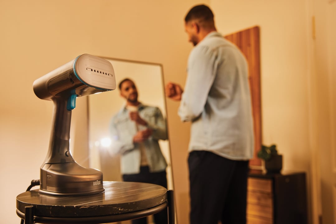 Garment steamer on a table with a man getting dressed in the background