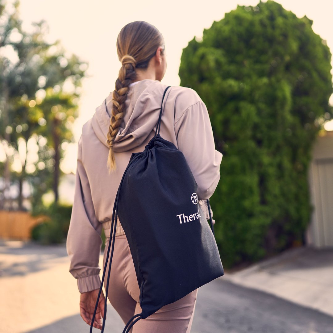 Woman with a braided ponytail walking outdoors with a black drawstring bag