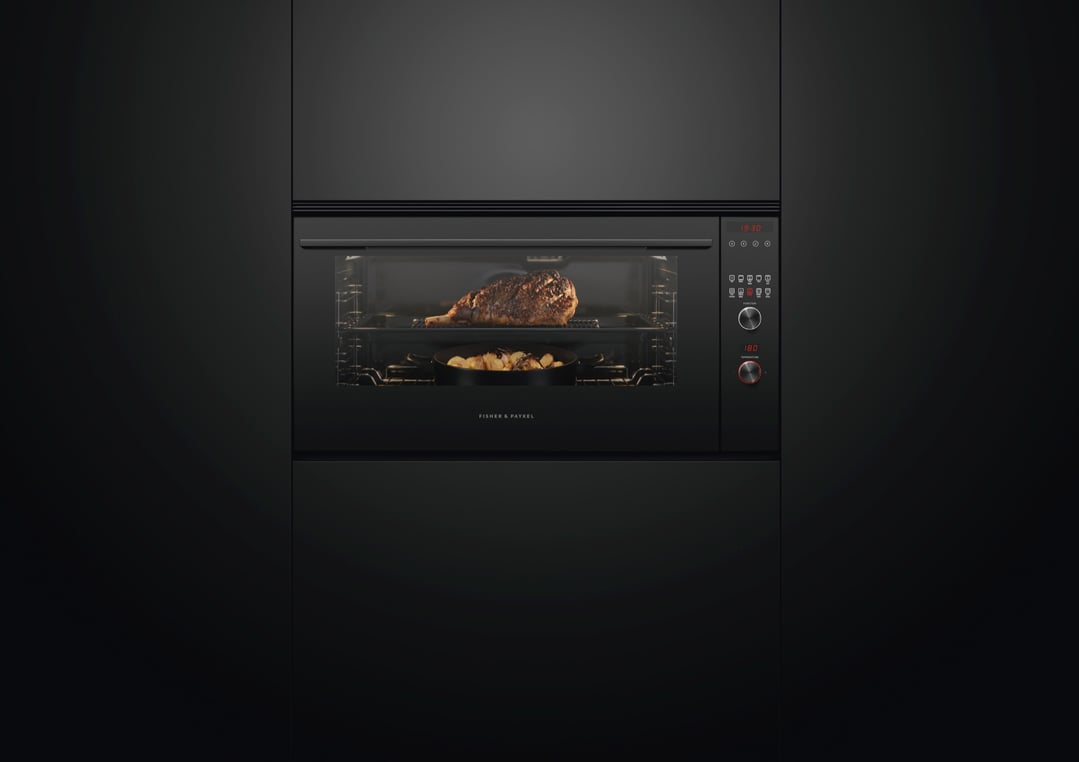 Built-in oven cooking a large roast and potatoes in a dark kitchen