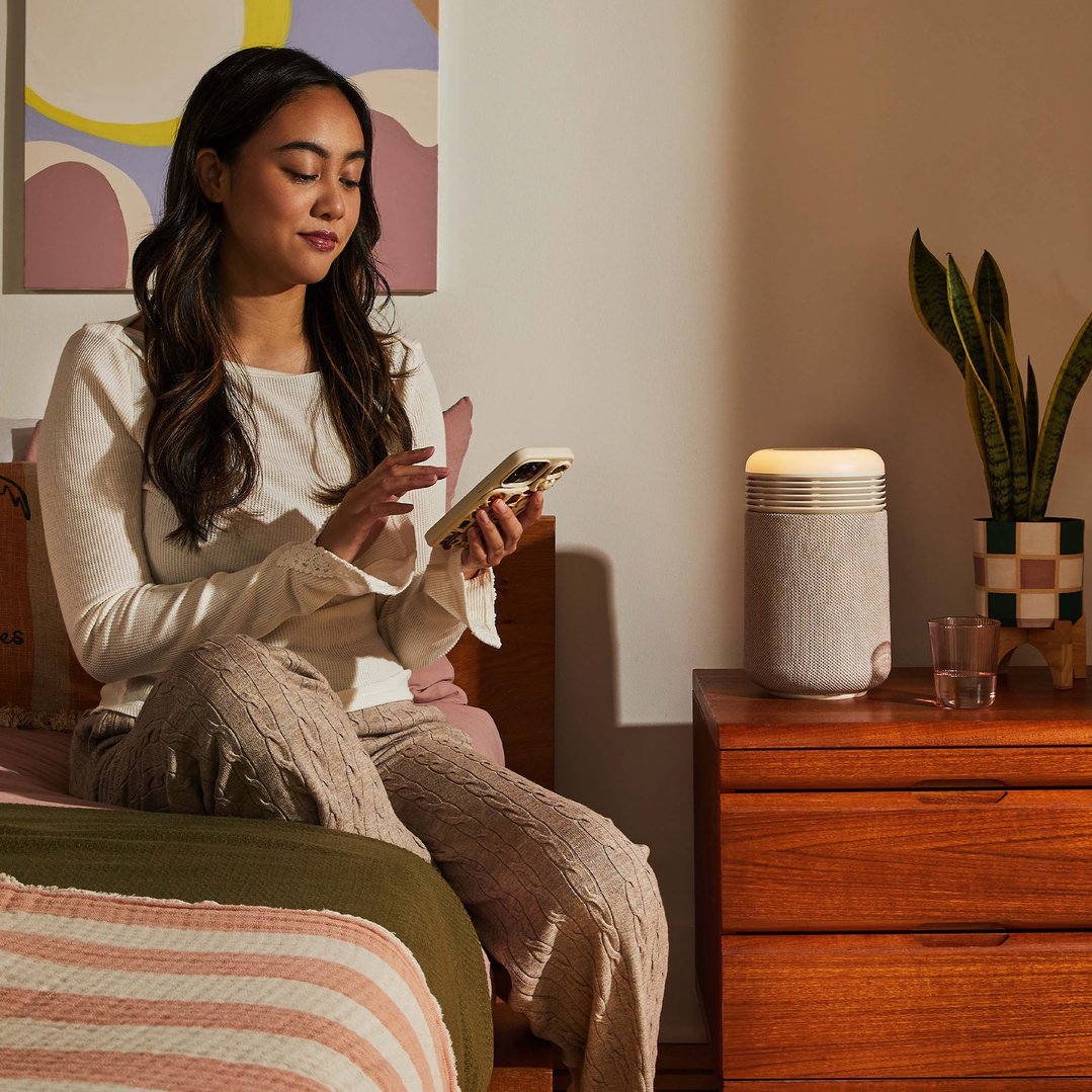 Woman sitting on a bed using a phone next to an air purifier