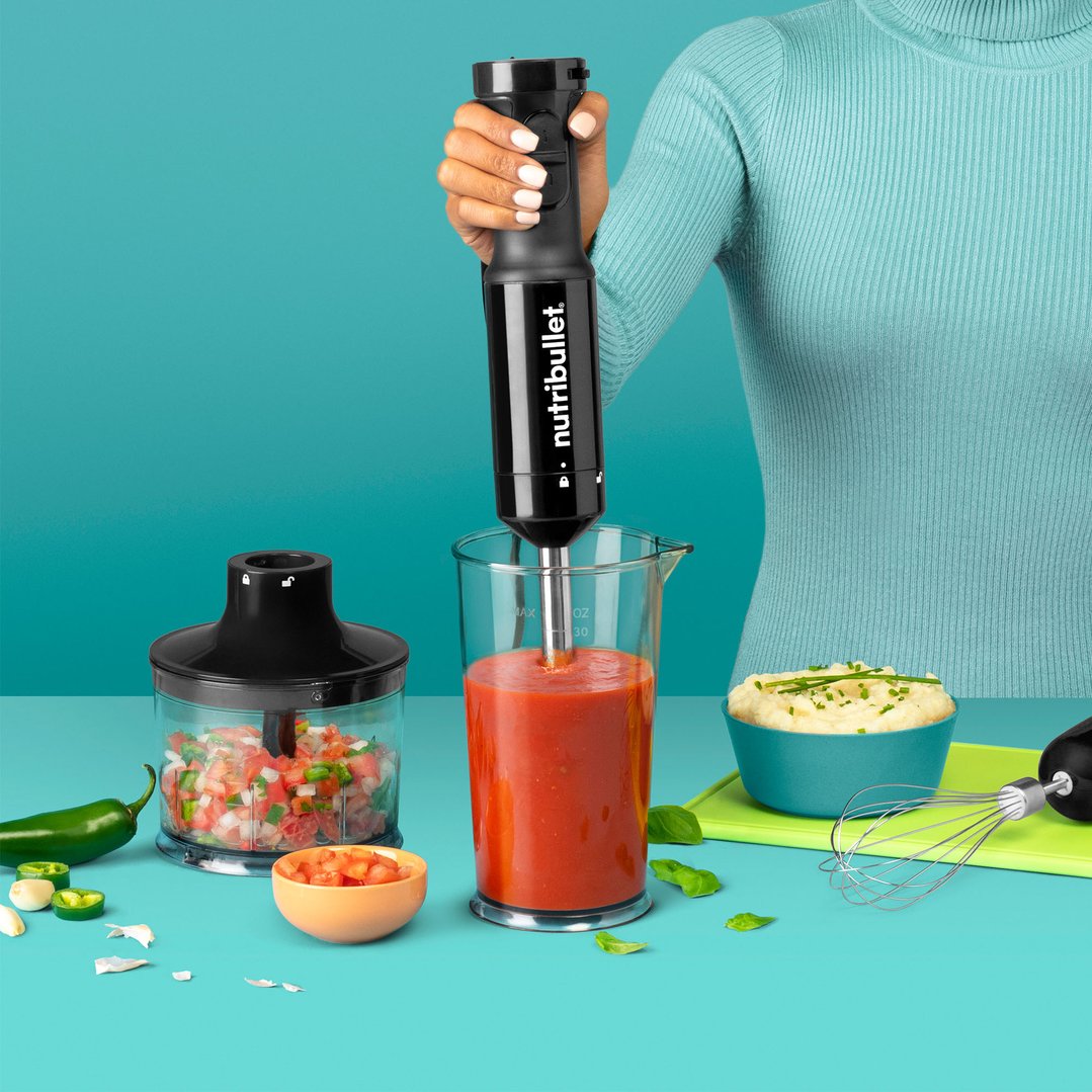 Woman using a Nutribullet Immersion Blender to blend tomatoes in a measuring cup