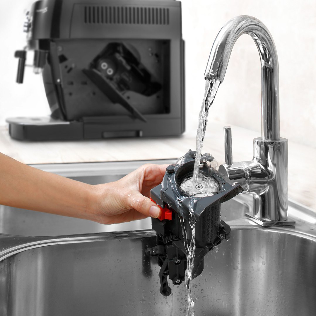 Hand rinsing a coffee machine component under running water in a kitchen sink