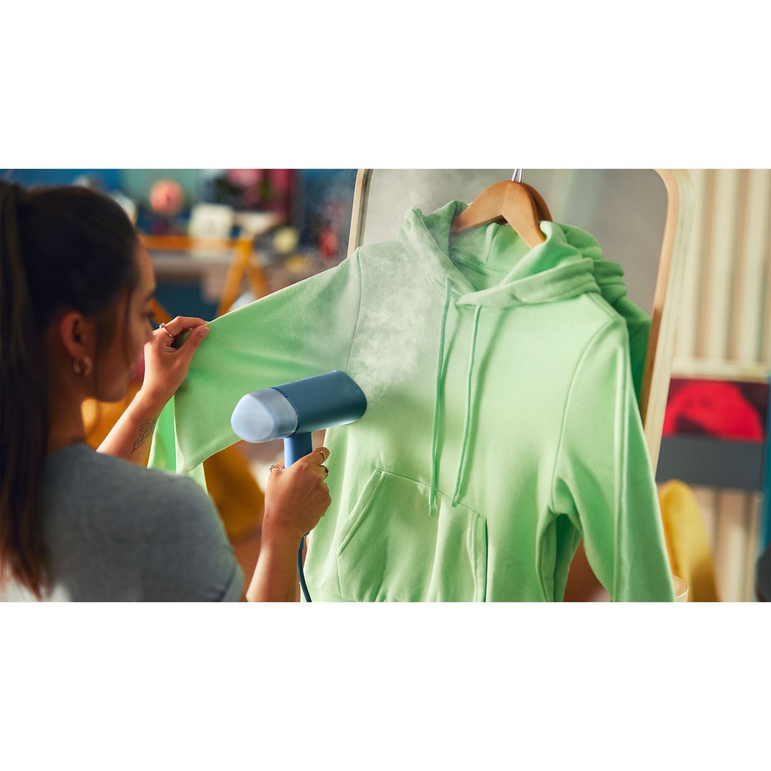 Woman using a Philips Garment Steamer to steam a light green hoodie
