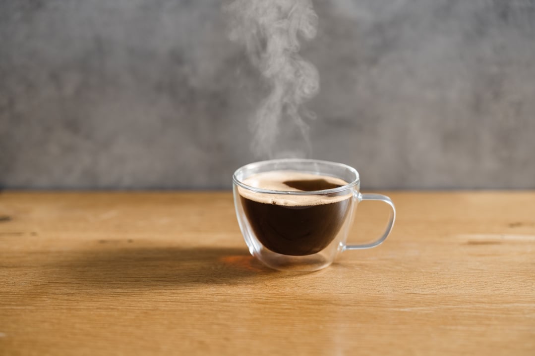 Steaming hot coffee in a clear glass mug on a wooden surface