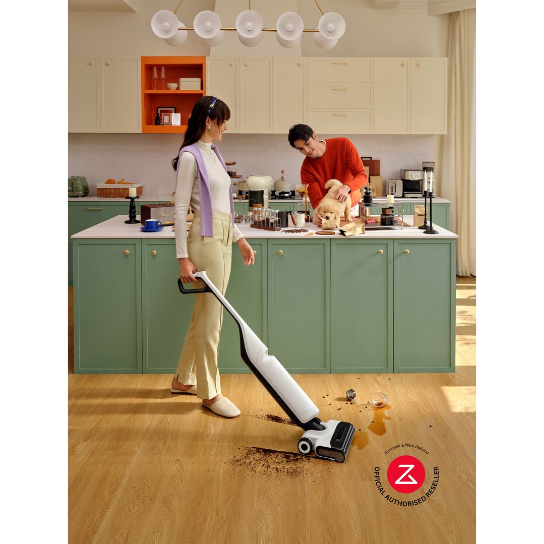 Woman using a Roborock vacuum cleaner in a kitchen with a man and dog