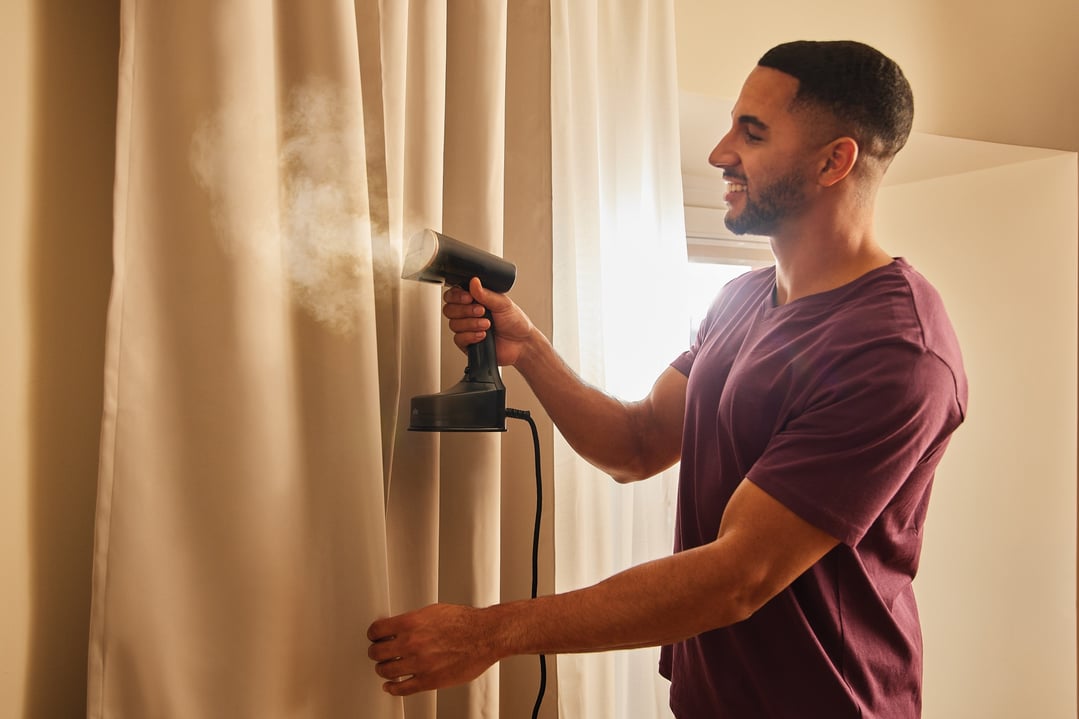 Man steaming curtains with a Braun Garment Steamer in a sunlit room