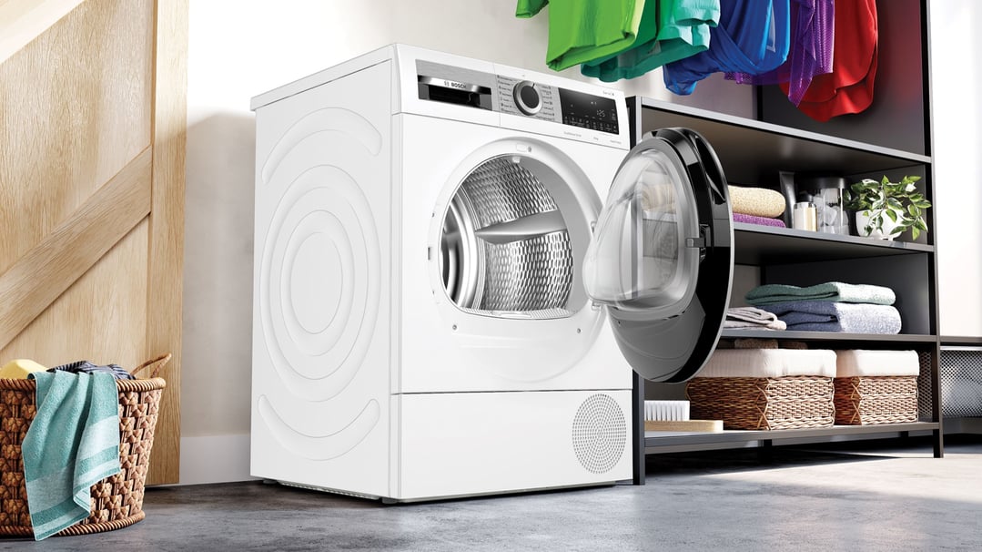 White Bosch heat pump dryer with door open in a laundry room setting