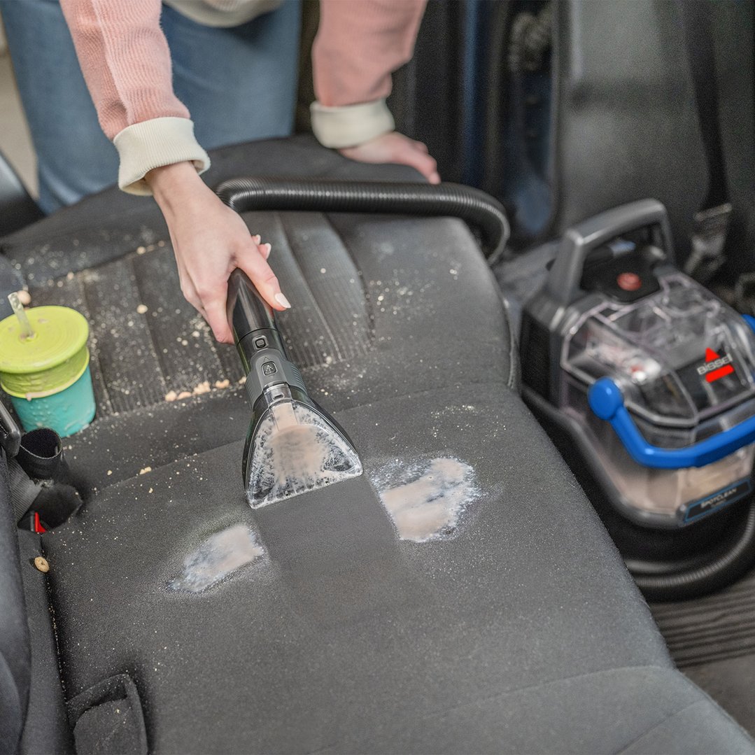 Woman cleaning car seat with a BISSELL SpotClean vacuum cleaner