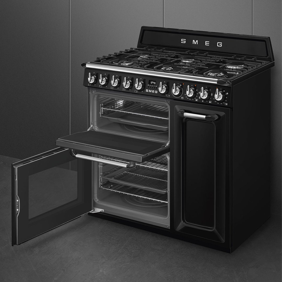 Black freestanding dual fuel oven/stove with open doors in a dark kitchen