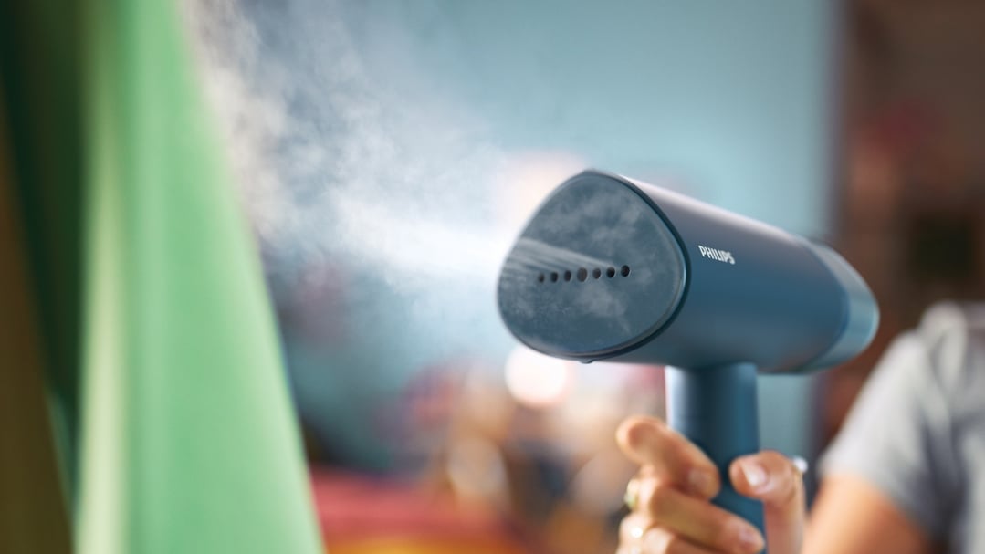 Hand holding a Philips handheld garment steamer emitting steam