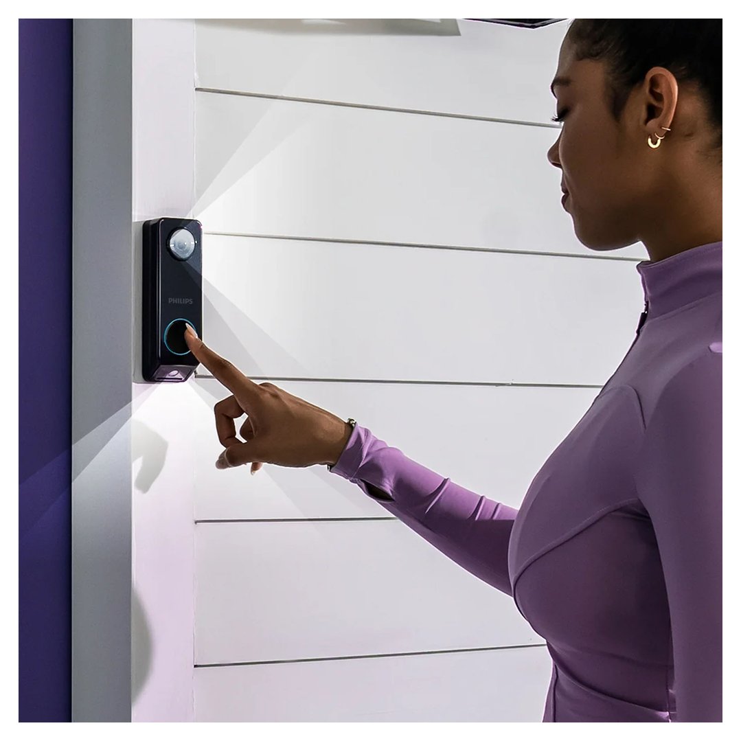 Woman pressing the button on a Philips video doorbell on a white wall