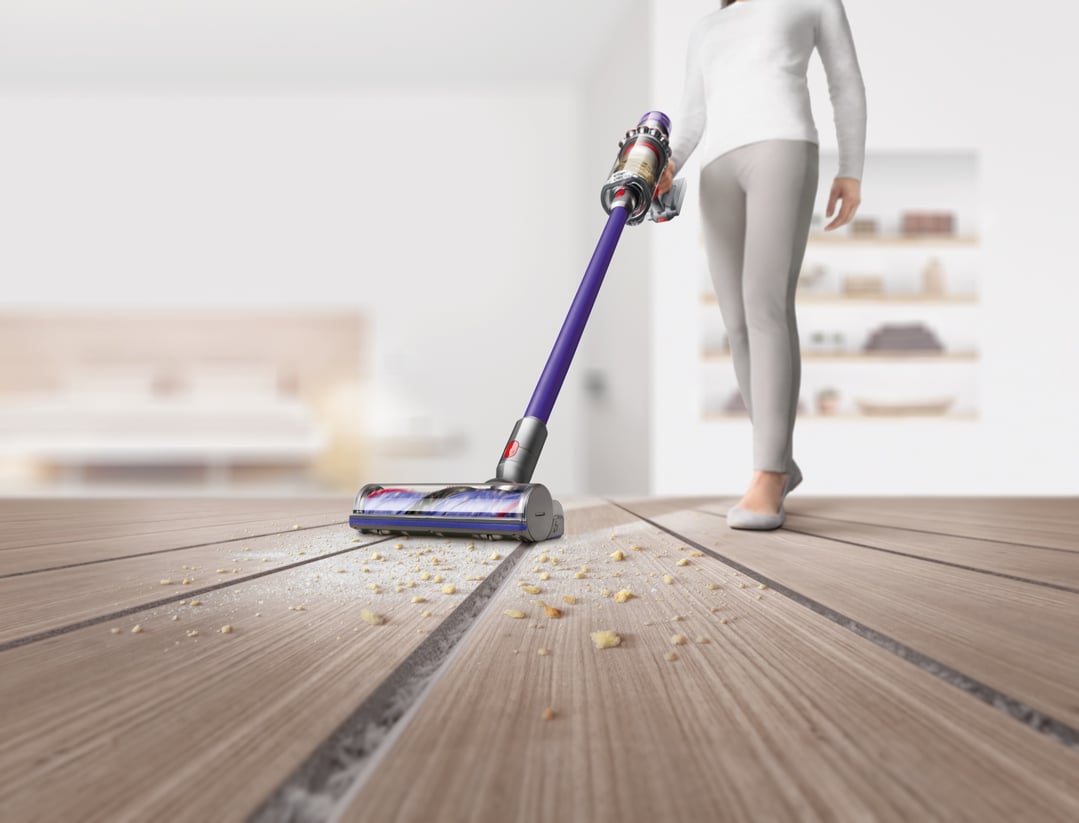 Woman vacuuming crumbs and dust from a wooden floor with a Dyson V11 stick vacuum