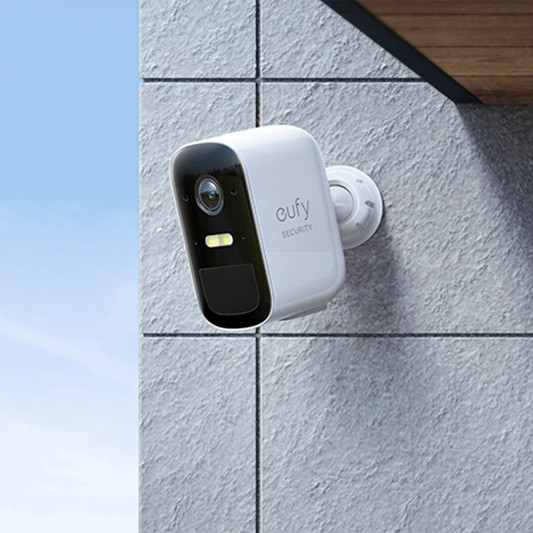White eufy security camera mounted on a grey tiled wall outdoors