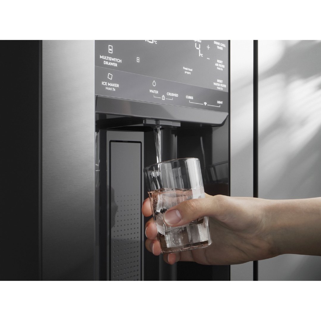 Hand holding a glass of water and ice being dispensed from a fridge
