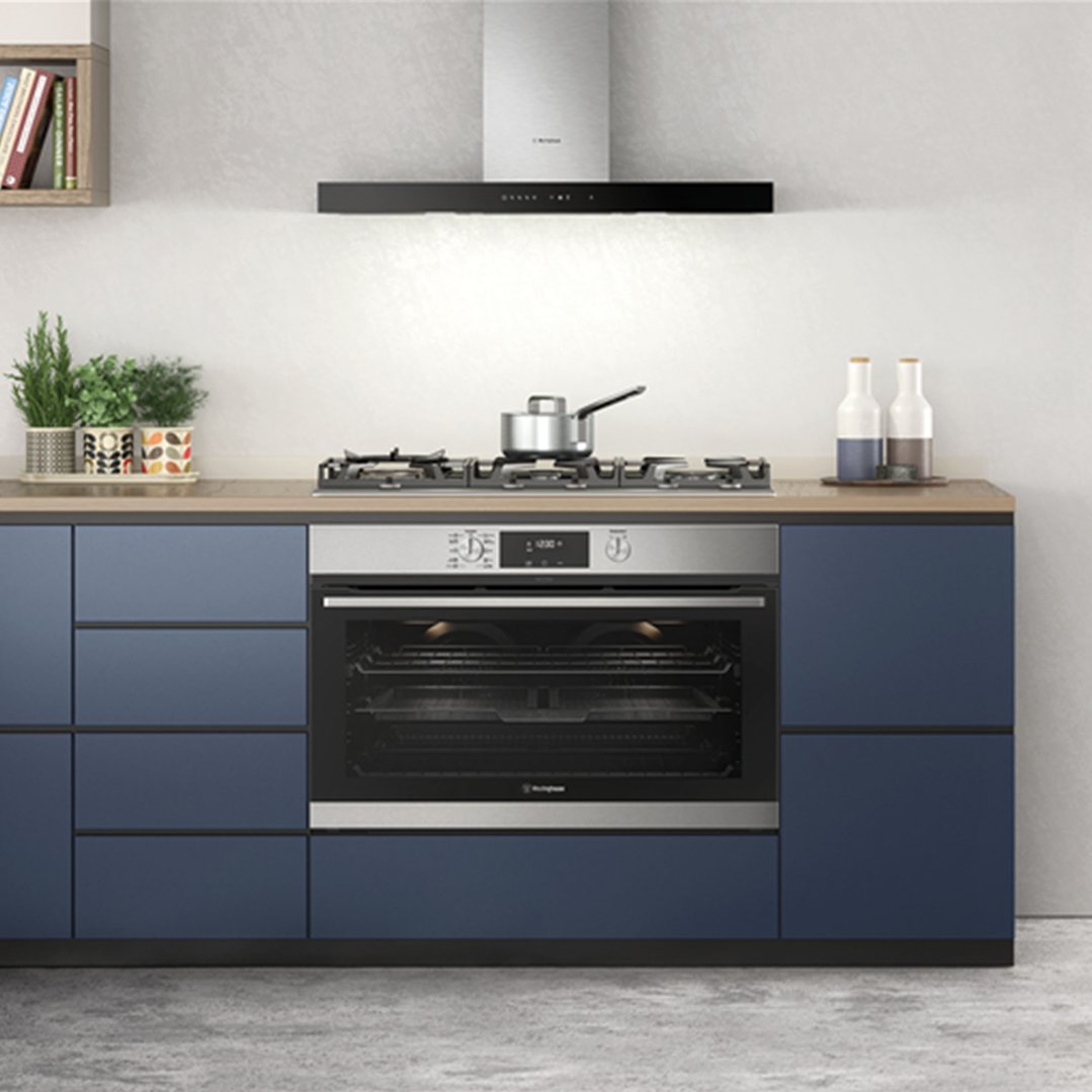 A gas cooktop and oven built into blue kitchen cabinetry with a rangehood