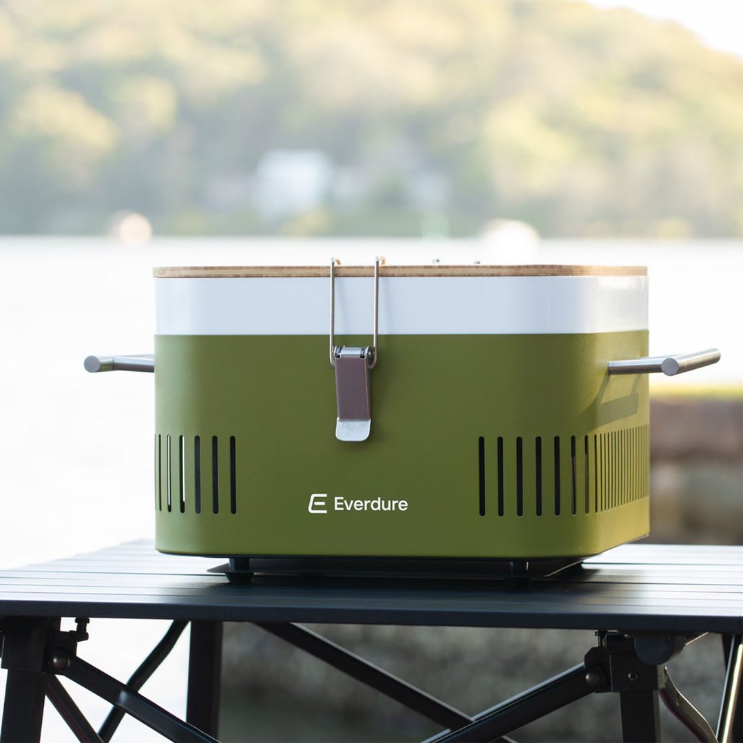 Portable charcoal BBQ on a black table outdoors with a blurred natural background