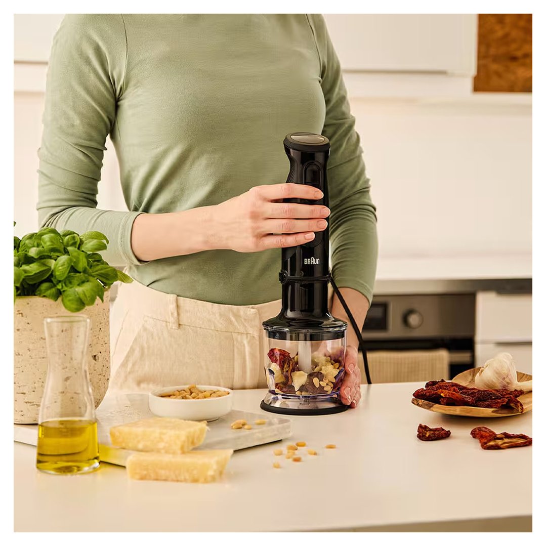 Person holding a Braun hand blender with ingredients in a kitchen setting