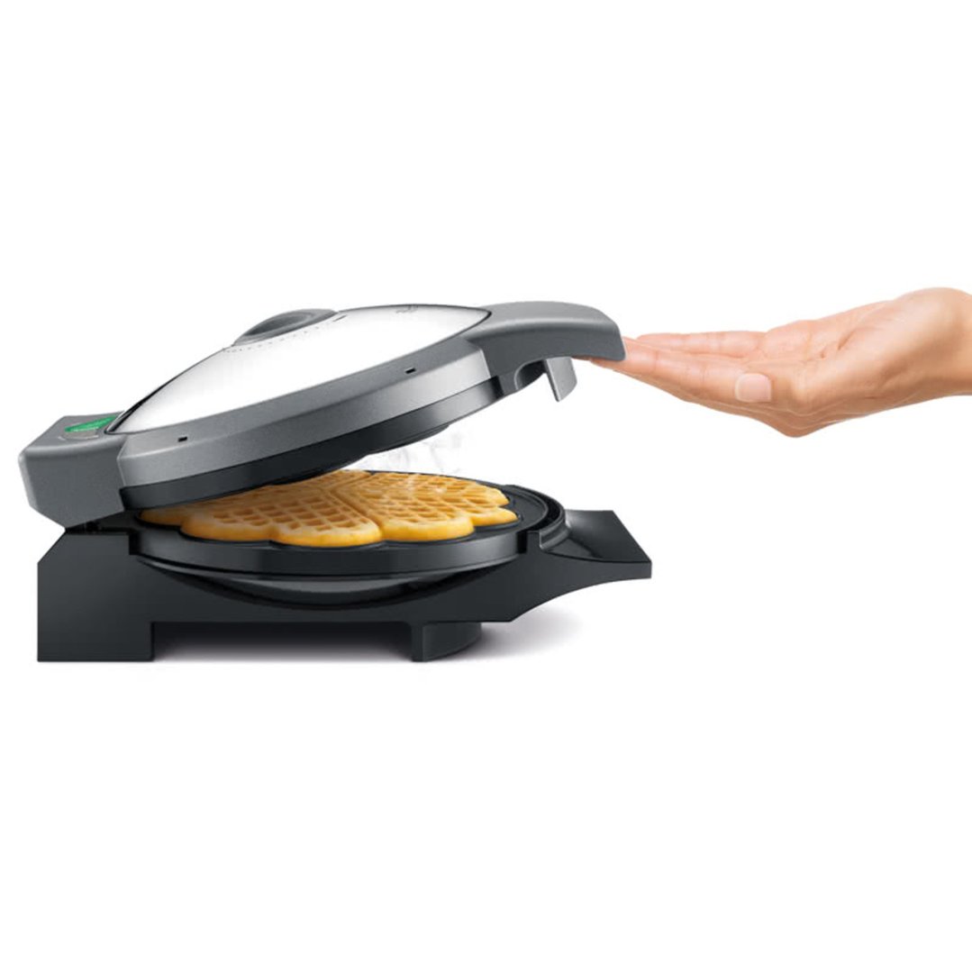 Hand reaching for a Breville waffle maker with a heart-shaped waffle inside