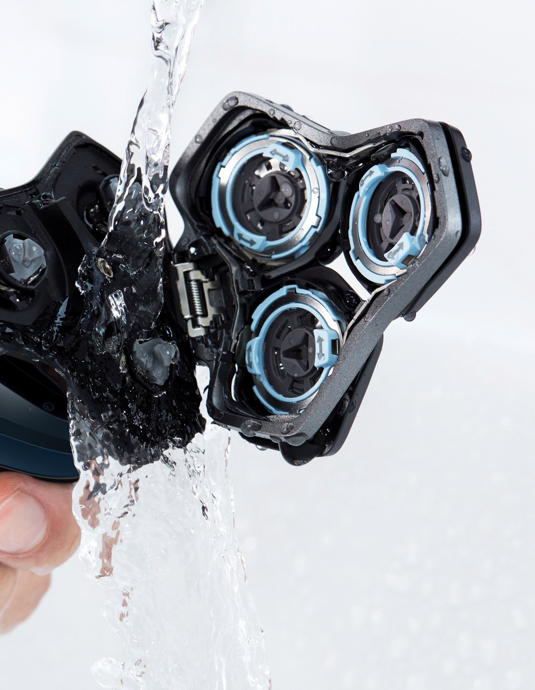 Hand holding a shaver under running water, cleaning the shaver head