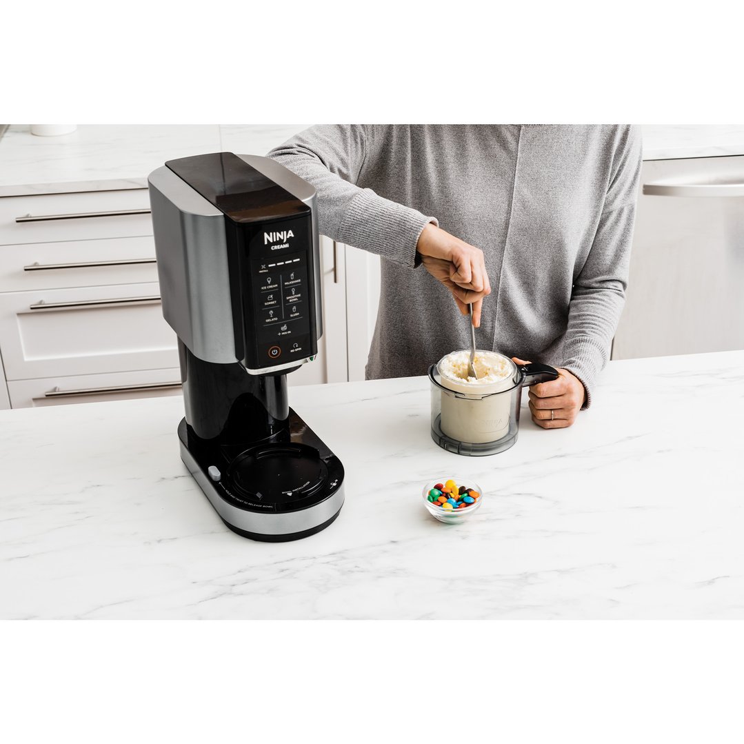 Person stirring ice cream in a Ninja CREAMi ice cream maker on a kitchen counter