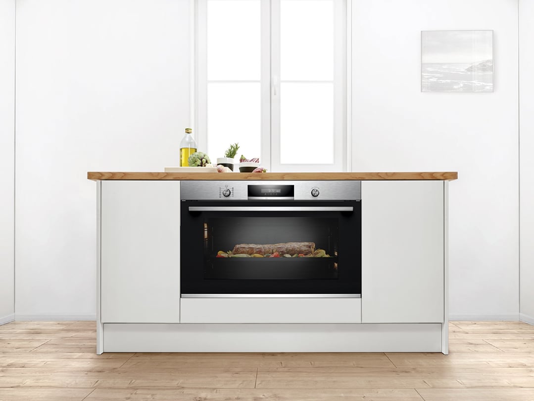Built-in oven cooking a roast with vegetables in a modern kitchen setting