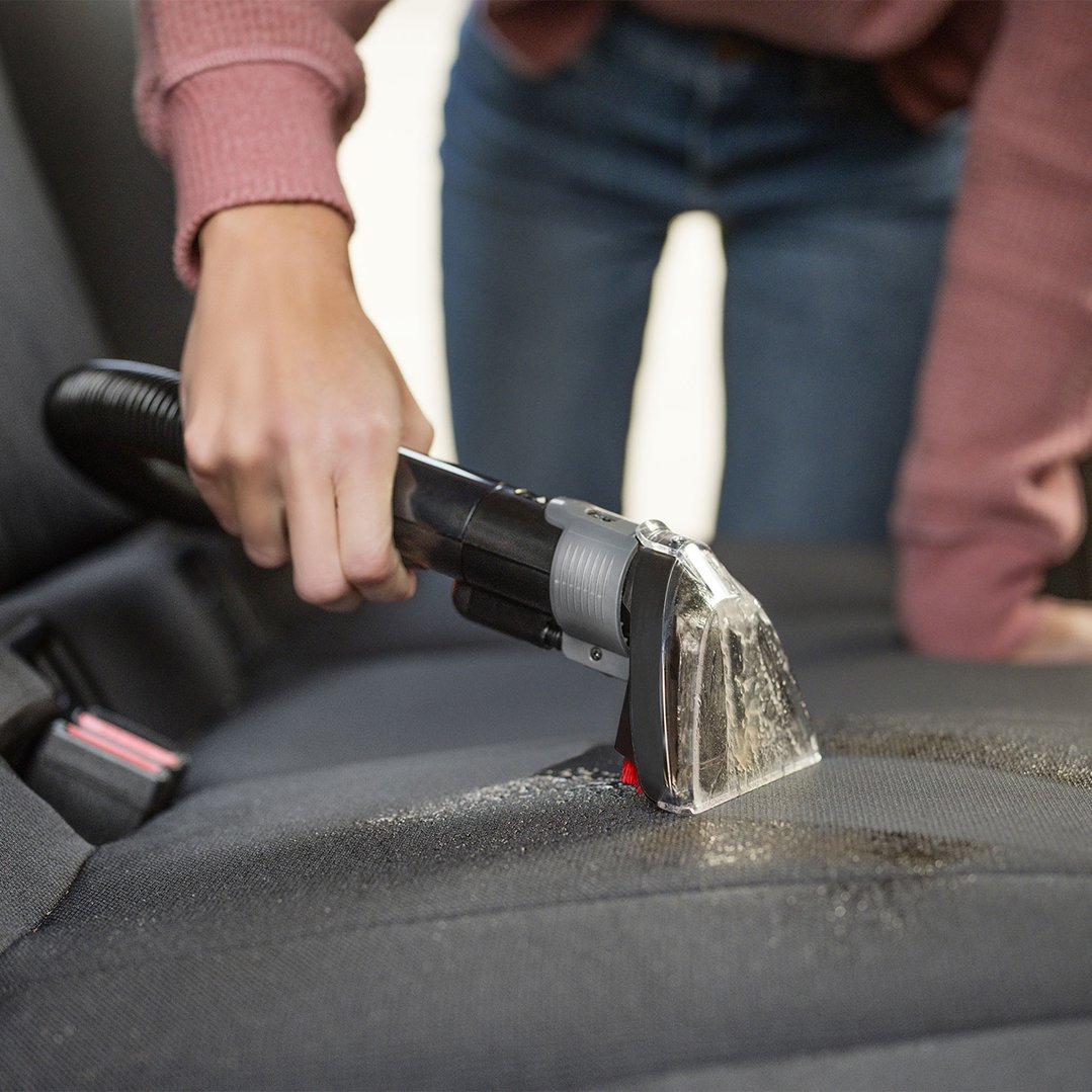 Person cleaning a car seat with a BISSELL SpotClean vacuum cleaner