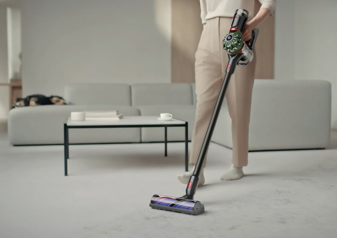 Woman vacuuming a light-colored floor with a Dyson handstick vacuum in a living room